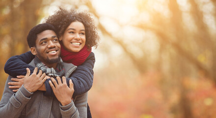 Autumn leisure and love concept. Couple in love walking in park, man giving piggyback ride to...