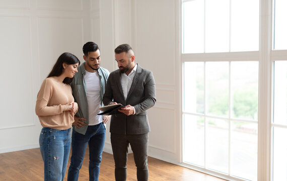 Young married Middle Eastern couple discussing agreement with real estate agent or broker. Professional financial advisor or salesman explaining contract details with millennial clients at meeting