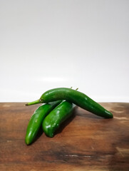 high angle close-up shot of three green chilies on a rustic wooden cutting board with a white background.