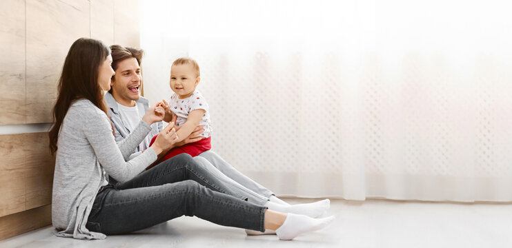 A young family, consisting of a mother, father, and toddler, sit together on the floor of a modern home. The parents are smiling at their child, who is sitting on the fathers lap, copy space - Powered by Adobe