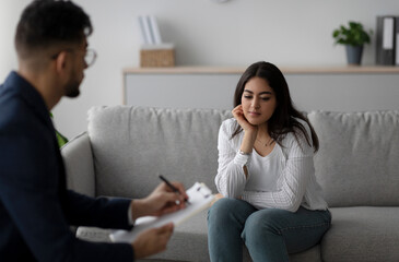 Fototapeta premium Psychological help service. Depressed arab woman having psychotherapy session with counselor, consulting professional therapist at mental health clinic.