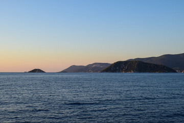 Beautiful island landscape at sunset with lush, thick woodland and turquoise tropical waters. Mountains, dense green forests, white rocks and clear blue waters make up the idyllic travel destination.