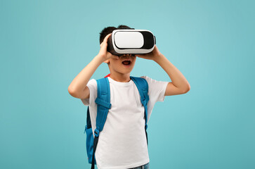 Portrait Of Excited Little Asian Schoolboy Experiencing Virtual Reality In VR Glasses Headset While Standing Over Blue Background In Studio, Korean Kid Enjoying Modern Technologies For Entertainment