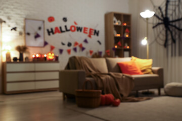 Interior of living room decorated for Halloween with sofa, shelf unit and glowing lamps in evening