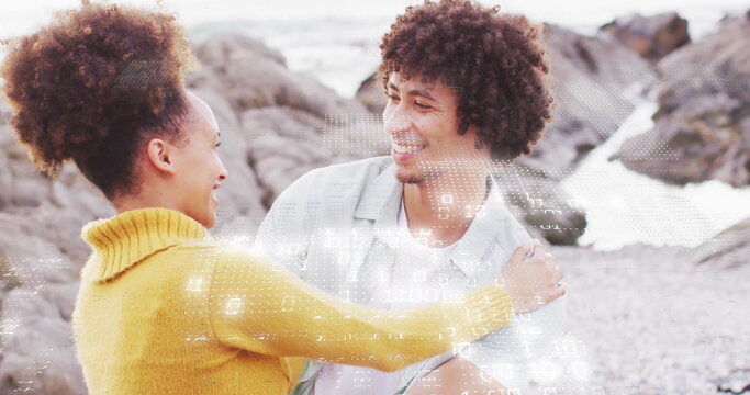 Laughing couple wearing mustard sweater and light grey shirt standing on rocky beach, with pebbles - Powered by Adobe