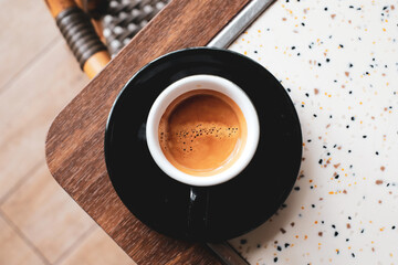 Top view of a freshly brewed espresso served in a black cup on a wooden table with terrazzo...