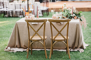 Rustic wedding set, vintage dining table with decorations, flowers, boho style, event, party or wedding. Wooden chairs, linen tablecloth, candles, accessories and glasses on newlywed desk on lawn