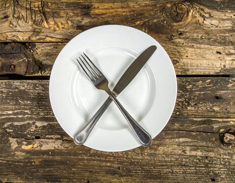 Empty white plate with crossed fork and knife on rustic wood - Powered by Adobe