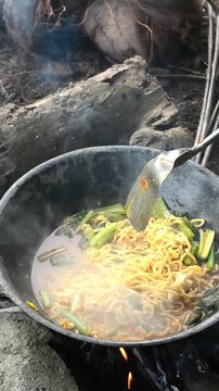 A person cooking traditional Indonesian seblak in the middle of a lush rice field, combining authentic street