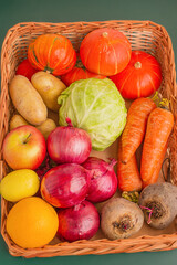Vegetables and fruits in a wicker box on a green background.