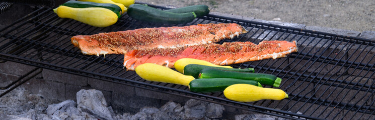 King salmon filets with teriyaki sauce and sesame seeds grilling on an outdoor barbeque pit, along...
