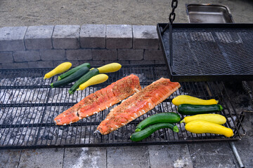 King salmon filets with teriyaki sauce and sesame seeds grilling on an outdoor barbeque pit, along...