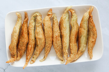 Closeup of a plate of freshly made and fried Indonesian Otak-Otak Goreng (Fried fish cakes), crispy and golden brown, arranged on a white serving dish.