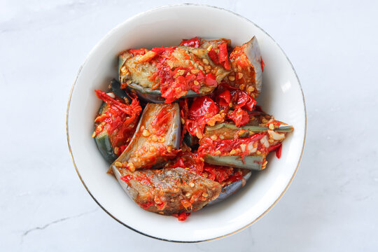 Top view of a plate of fried eggplant tossed in a vibrant and spicy red chili sauce.
