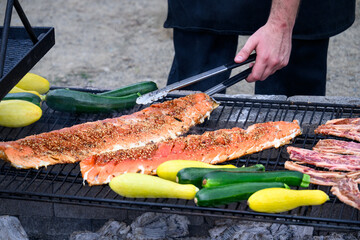 Chef using tongs to move cooking king salmon on an outdoor barbeque grill to cook along with Korean...