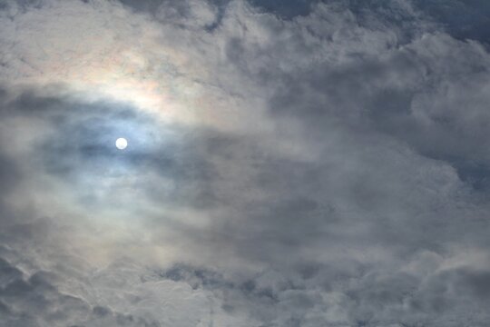 Dramatic clouds partially cover the sun, creating a glow where the round shape of the sun is faintly visible from a distance, adding depth and atmosphere to the sky.