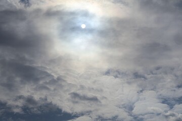 Dramatic clouds partially cover the sun, creating a glow where the round shape of the sun is faintly visible from a distance, adding depth and atmosphere to the sky. time lapse