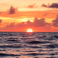 Captivating ocean sunset with a brilliant orange sun partially submerged. The sky is ablaze with warm hues and dramatic clouds, contrasting with the dark, textured sea.