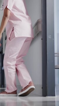 Vertical video: Nurse pausing at handrail in hospital corridor is sliding into seated squat to rest