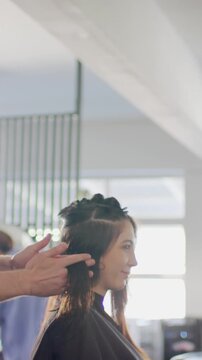 Vertical video: Hairstylist unclipping side section while smoothing hair to check length at salon