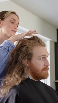 Vertical video: Hairdresser draping, parting and lifting male client hair to shape volume in salon