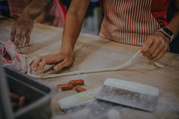 Hands shaping pretzel dough on a floured wooden table. Twisting and forming traditional pretzels before baking, rustic homemade style and artisan preparation.