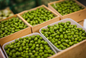 A variety of green peas are neatly arranged in both wooden and plastic crates. The vibrant green color of the peas stands out, indicating their freshness and quality. 