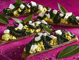 Three triangular toasts topped with spinach, egg, and cheese, garnished with flower-like sprinkles and bay leaves