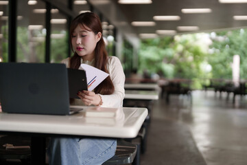 Obraz premium Asian woman freelancer works on laptop outdoors reviewing business report digital nomad lifestyle remote worker in modern open space productive work