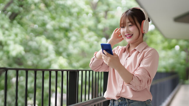 Young Asian adult woman enjoys serene outdoor moment with wireless headphones and smartphone embracing nature digital freedom