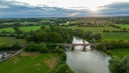 Fototapeta premium Sunset aerial landscape showcasing Oglio River winding near Pontevico, Italy, revealing verdant countryside, infrastructure, agricultural fields, and distant industrial structures