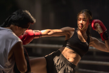 Confident female Muaythai boxer practicing Thai boxing with male trainer in gym