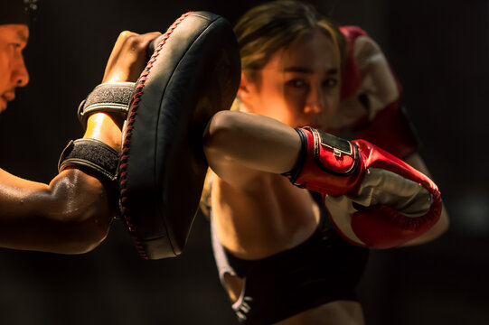 Confident female Muaythai boxer practicing Thai boxing with male trainer in gym - Powered by Adobe
