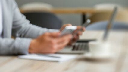 Person using a phone near a laptop and coffee cup on a table.