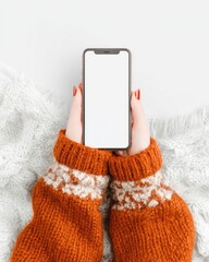Hands holding a phone, wearing an orange sweater, on a white blanket