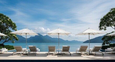 High-angle view of empty lounge chairs and white umbrellas by a tranquil turquoise ocean, conveying a serene and peaceful mood, with mountains in the background; a