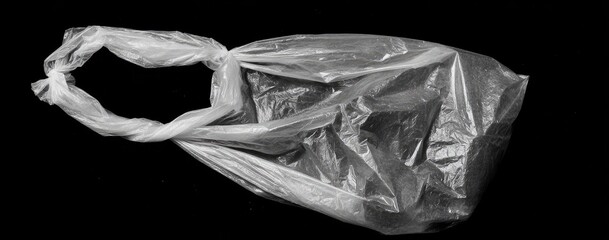 A single, crumpled, translucent plastic bag lies on a black background, its handle twisted