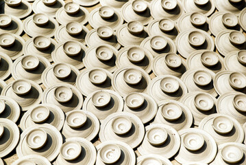 An artistic display of numerous handcrafted ceramic pottery pieces evenly arranged and lit by natural sunlight, showcasing traditional craftsmanship and detailing.