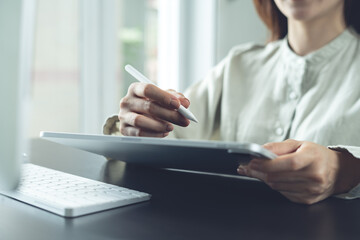 Closeup, business woman hand holding stylus pen, using digital tablet and working on laptop computer on office desk. Graphic designer designing creative project on tablet pc, online working