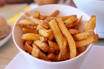 Golden, crispy homemade French fries served in a white bowl on a restaurant table, close-up view. Perfect comfort food or fast food concept with natural lighting.