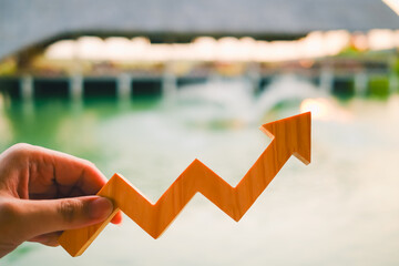 Hand holding wooden upward arrow graph symbolizing business growth, financial success, performance...