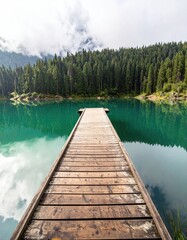 Obraz premium Wooden dock stretching into a tranquil alpine lake, surrounded by towering pine trees and misty mountains