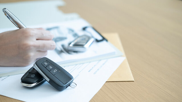 Car remote keys and pen with contract papers showing the process of auto sales deal paperwork and business transaction