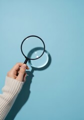 Hand Holding Magnifying Glass Against Light Blue light blue background