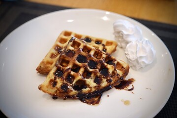 Waffle with chocolate syrup on top served on a white plate