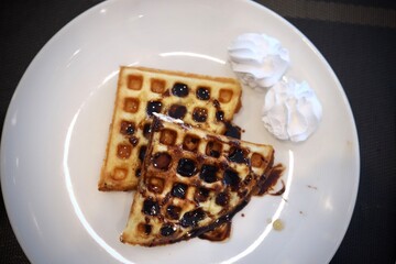 Waffle with chocolate syrup on top served on a white plate