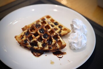 Waffle with chocolate syrup on top served on a white plate