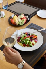 Fancy salad served on a white plate with champagne glass on the side in a restaurant background