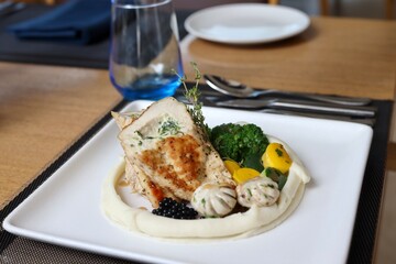 Grilled chicken with vegetables on the side served on a fancy white plate in a restaurant or cafe background 