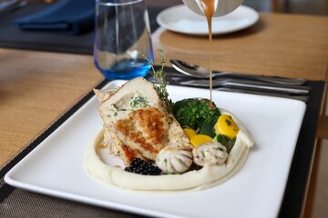 Grilled chicken with vegetables on the side served on a fancy white plate in a restaurant or cafe background 